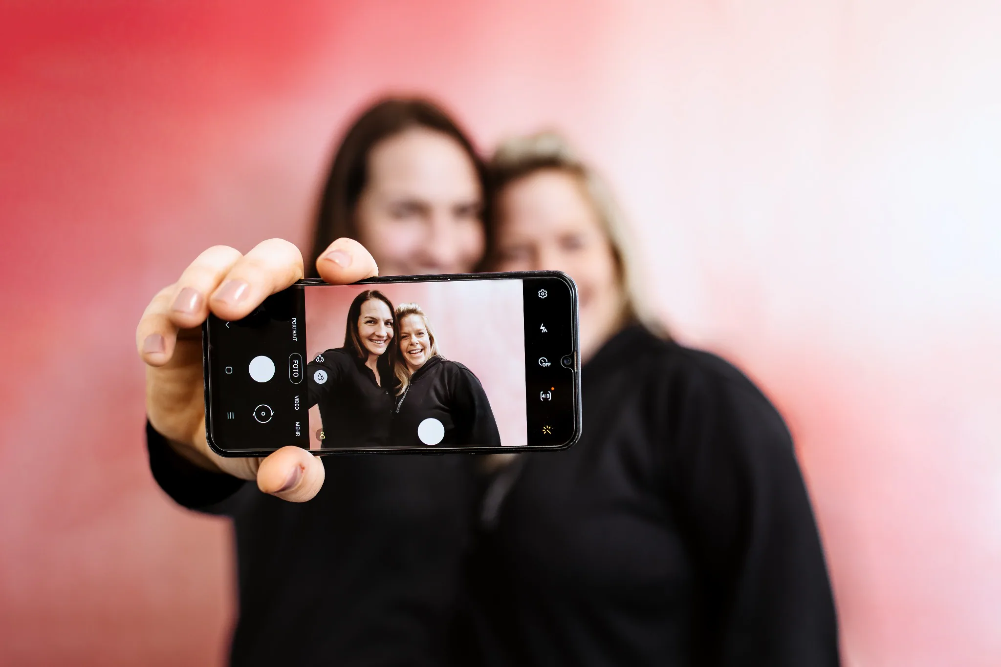 Zwei Frauen sind auf einem Smartphone-Display scharf zu sehen, während sie dahinter unscharf bleiben