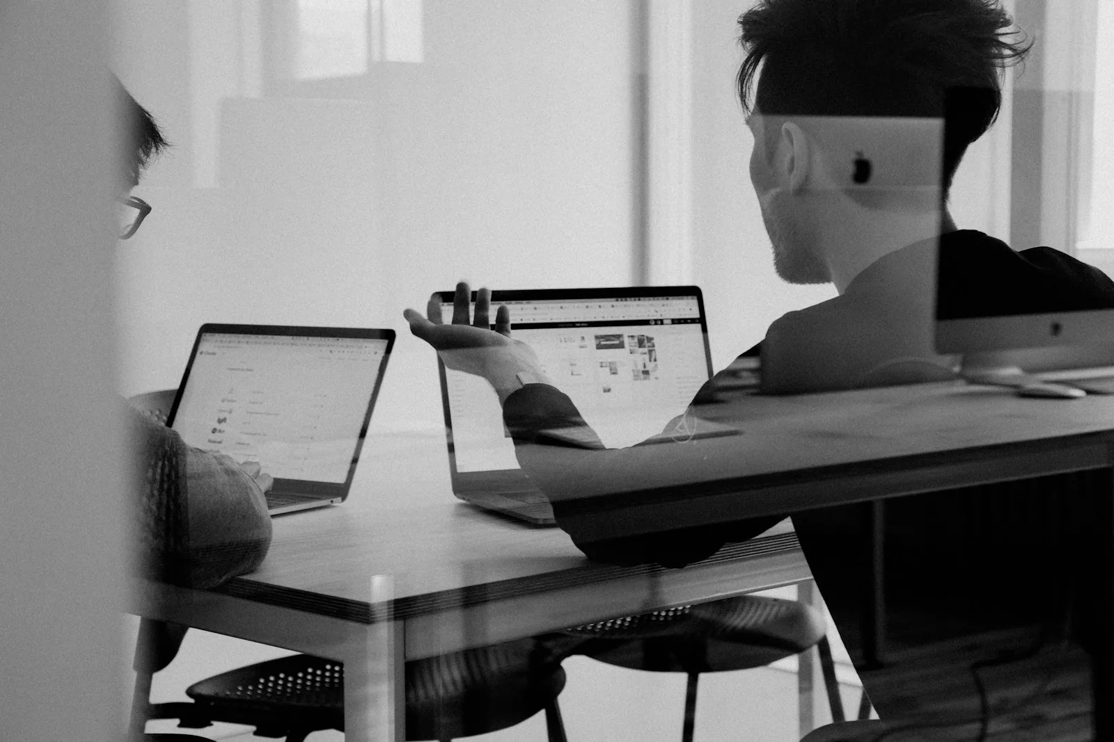 Zwei Personen besprechen eine Anwendung am Laptop hinter einer Glasscheibe.