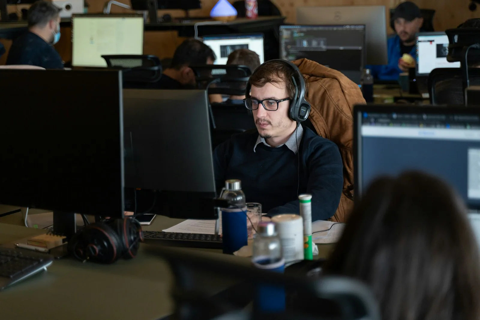 Ein Mann mit Brille und Kopfhörern arbeitet im Büro am Computer.