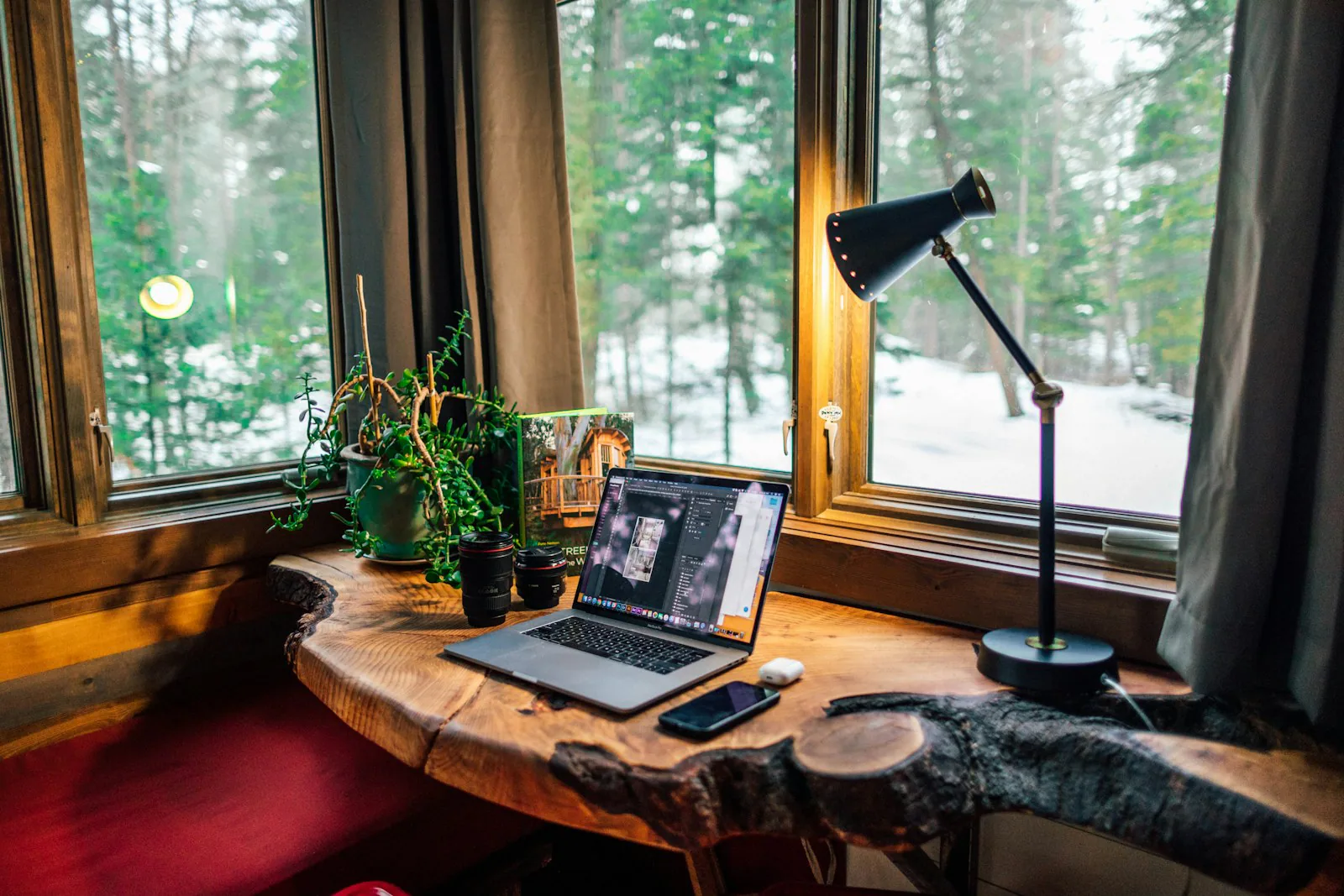 Ein Laptop steht auf einem Holzschreibtisch am Fenster mit Blick ins Grüne.
