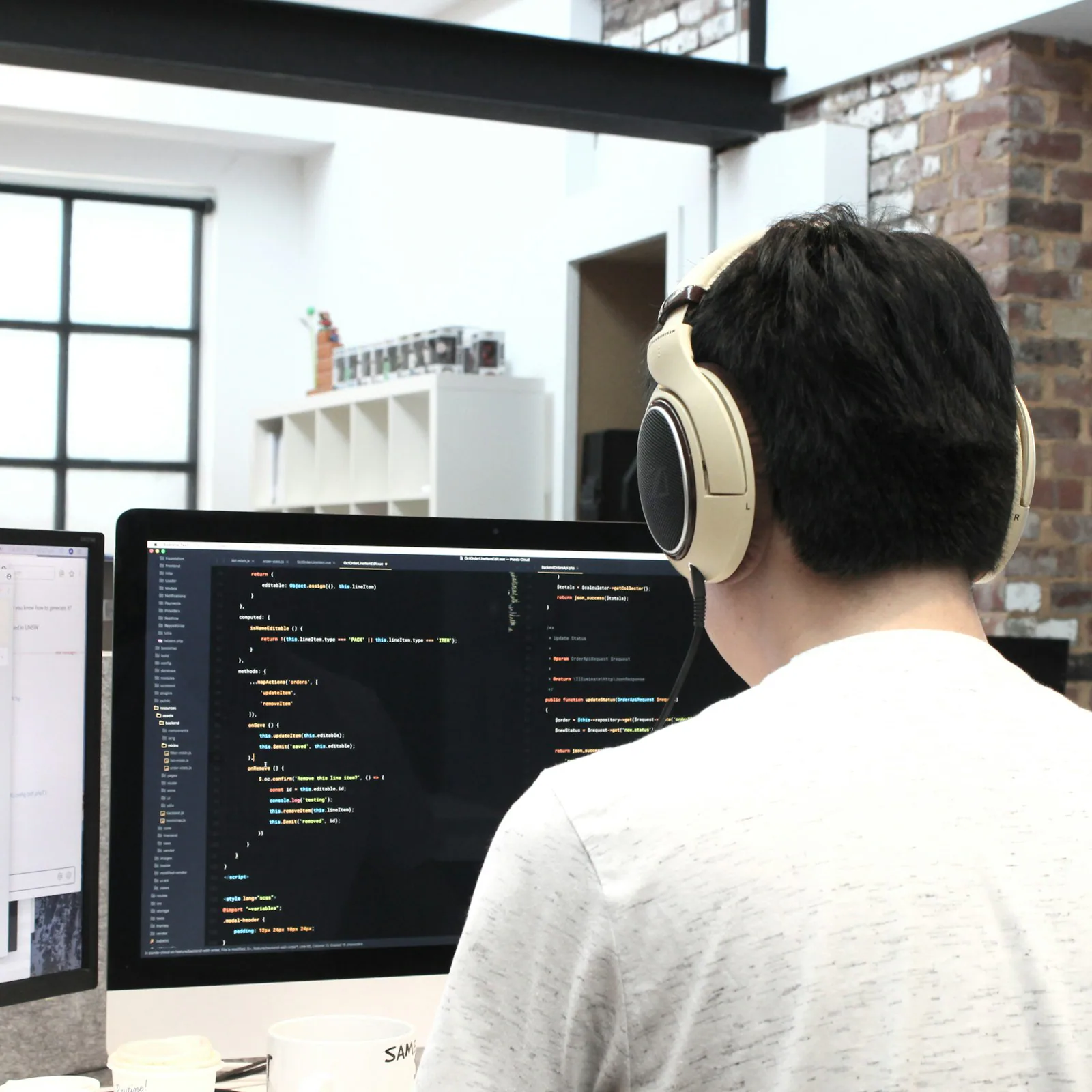 Ein Mann mit Kopfhörern arbeitet an zwei Bildschirmen mit Programmcode.