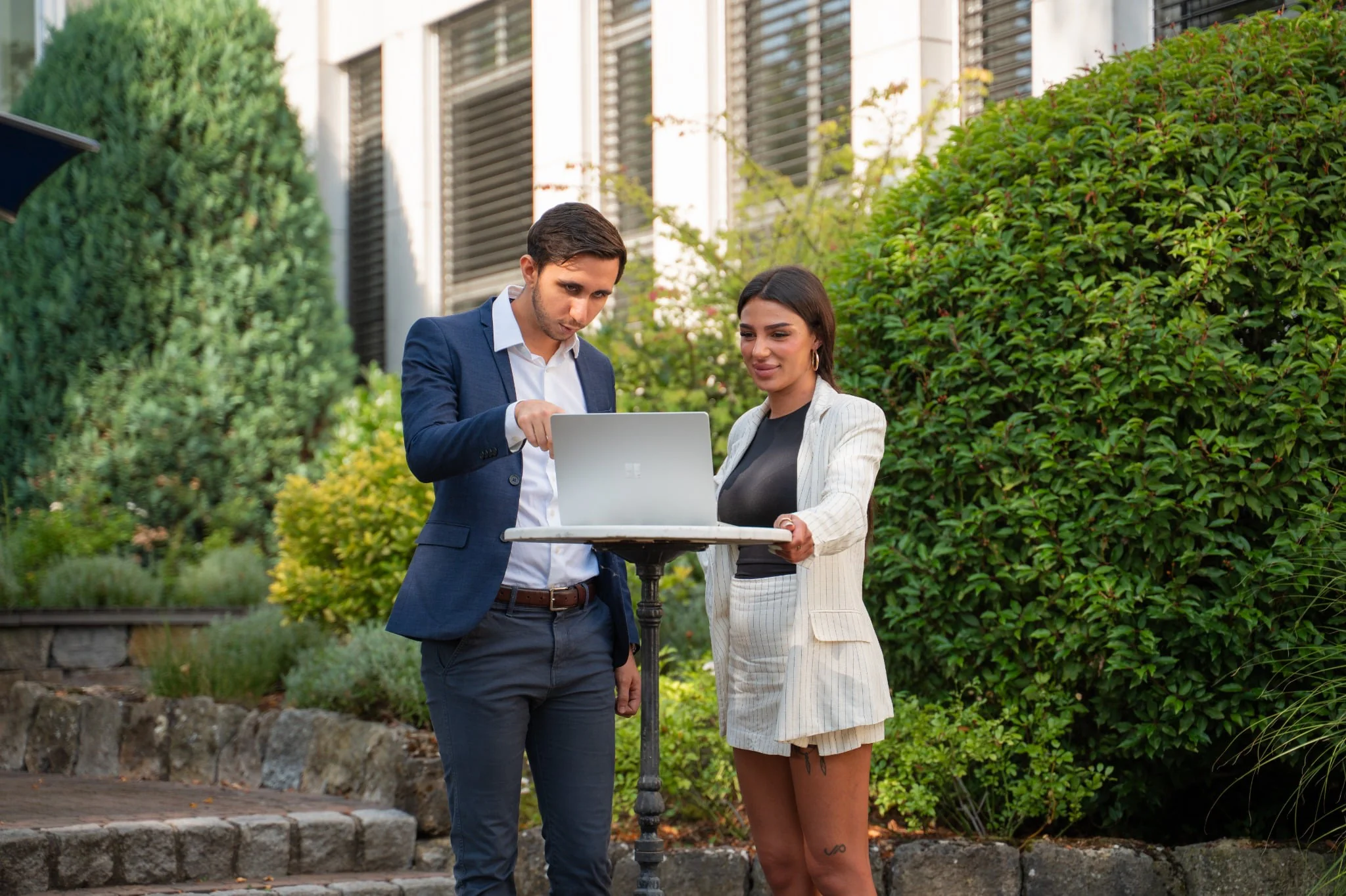 Zwei Menschen arbeiten gemeinsam an einem Laptop im Freien auf dem Campus