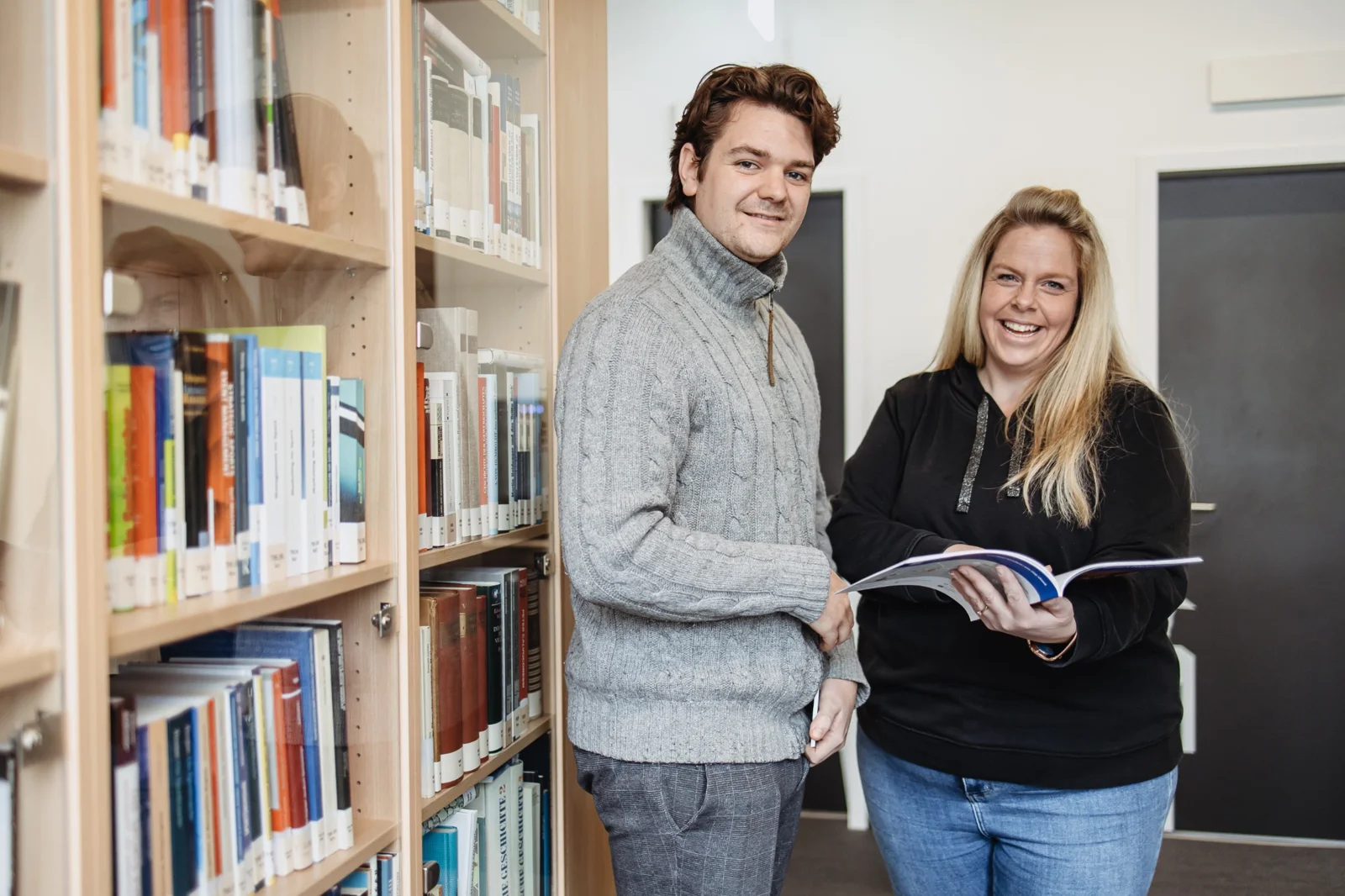 Zwei junge Menschen lächeln gemeinsam in der Campusbibliothek.