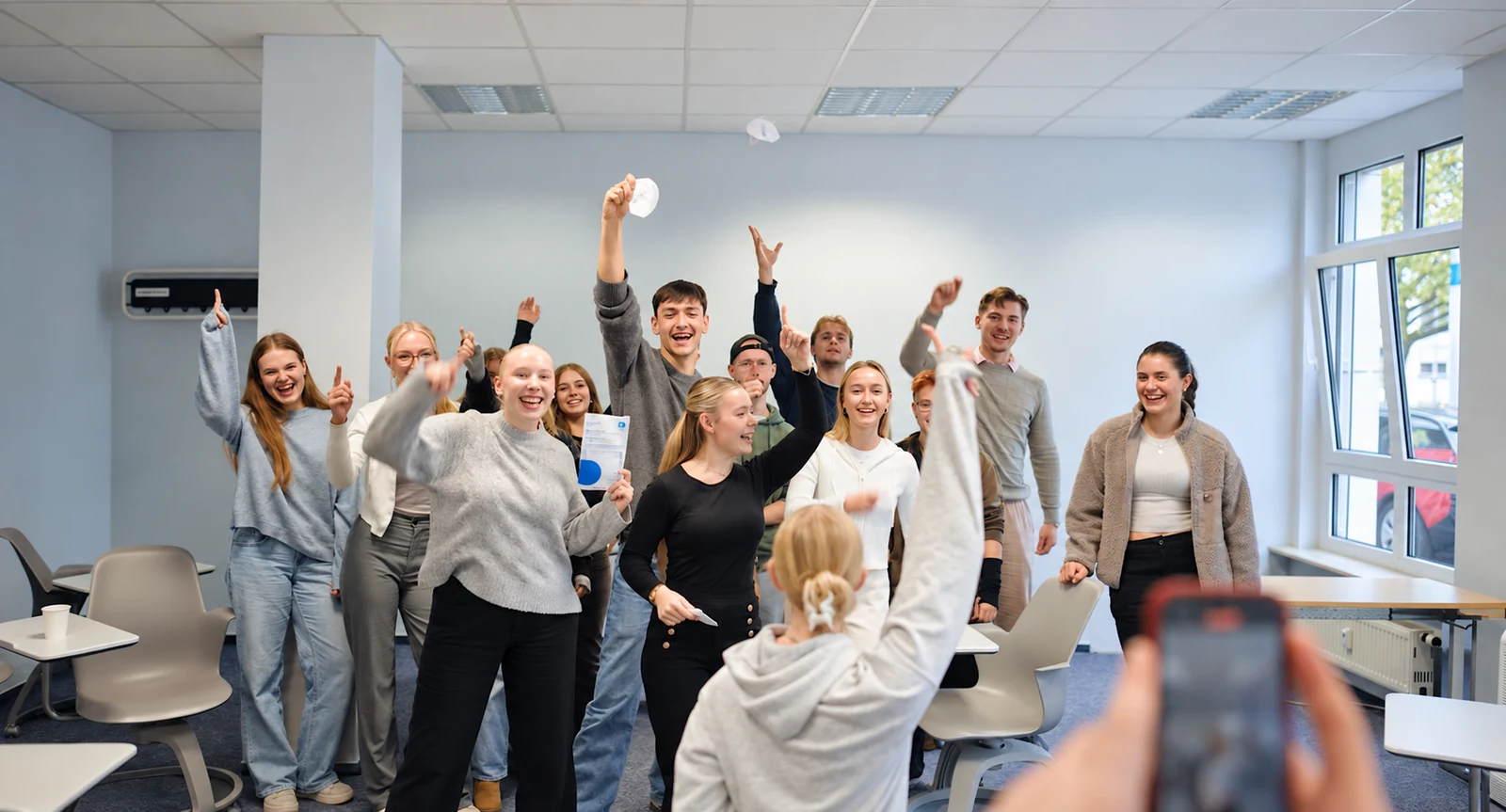 Eine Gruppe junger Studierender jubelt gemeinsam bei einer Campusveranstaltung im Seminarraum