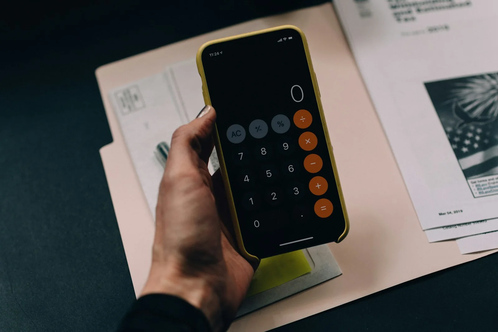 Eine Hand hält ein Smartphone mit geöffnetem Taschenrechner über Unterlagen.
