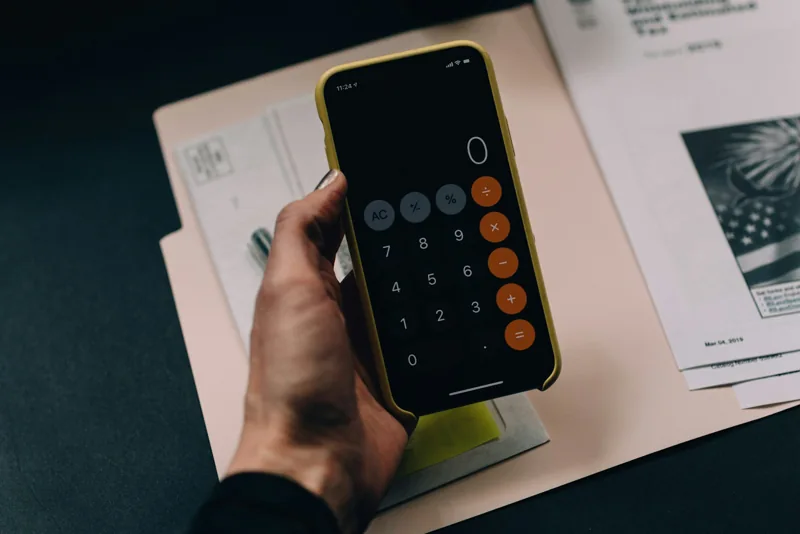Eine Hand hält ein Smartphone mit geöffnetem Taschenrechner über Unterlagen.