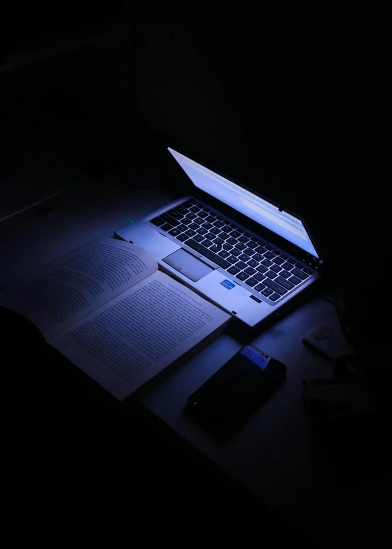 Ein Laptop neben aufgeschlagenen Büchern im blauen Licht.