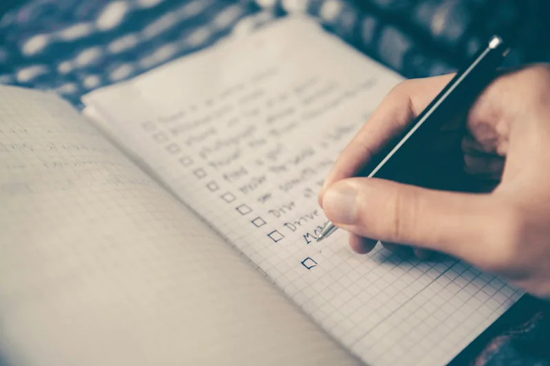 Eine Person schreibt eine Liste mit nächsten Schritten in ein Notizbuch.