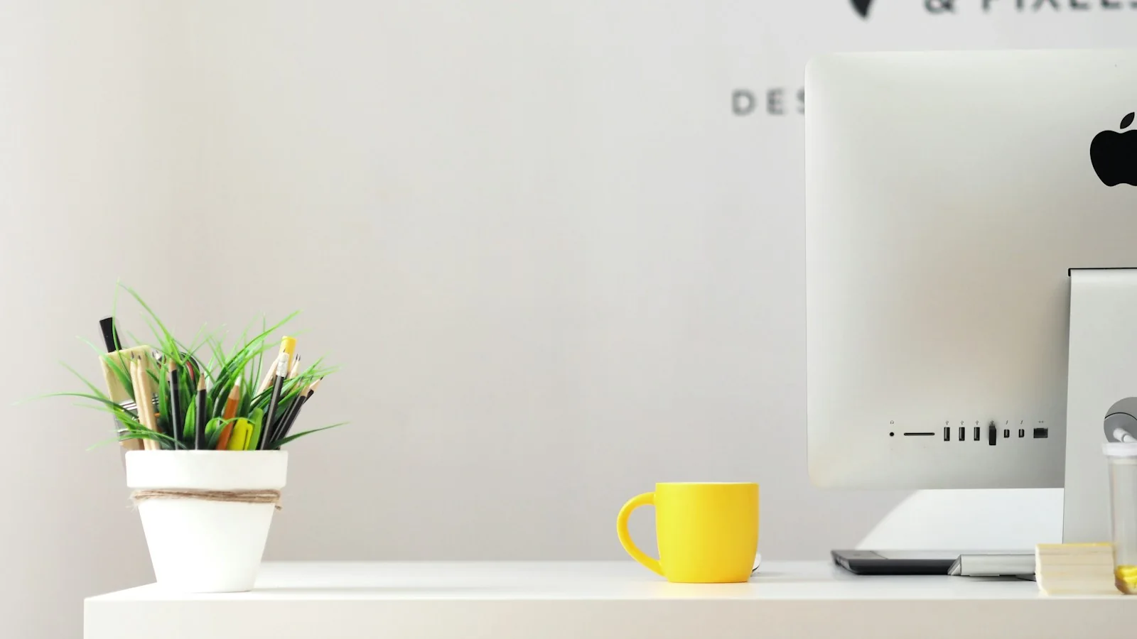 Ein heller Arbeitsplatz mit Computer, Pflanzen und einer gelben Tasse.