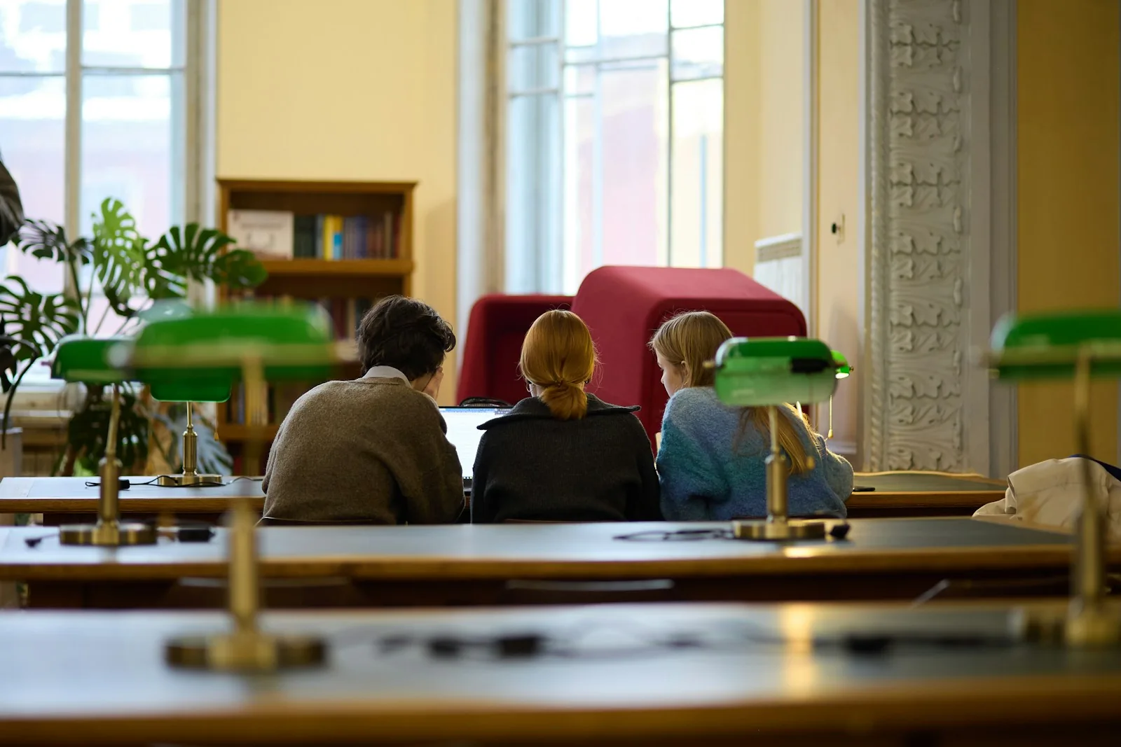 Drei Menschen lernen gemeinsam an einem Tisch in einer Bibliothek.