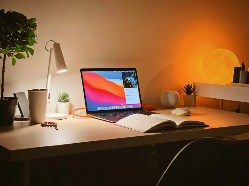 Ein beleuchteter Arbeitsplatz mit Laptop und aufgeschlagenem Buch.