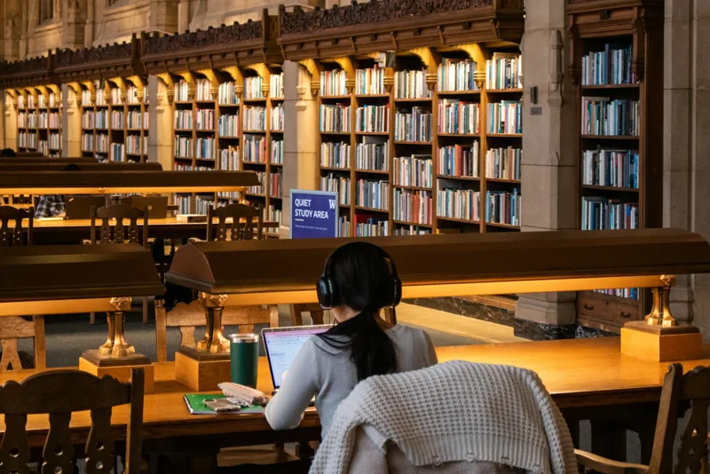 Eine Studentin arbeitet mit Kopfhörern in einer Bibliothek.